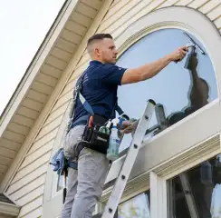 Professional window cleaner on a ladder using a squeegee to clean an exterior arched window, Portland, OR.